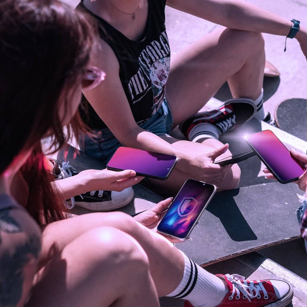 Drei Personen sitzen auf einer Skateboard-Rampe, jede hält ein Smartphone in der Hand und führt ein Gespräch. Sie tragen legere Kleidung und schaffen eine entspannte Atmosphäre.