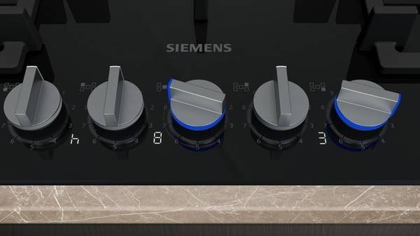 Nahaufnahme eines Siemens-Kochfeld-Bedienfelds mit fünf silbernen Brennerknöpfen, zwei davon angebracht um blaubeleuchtete Indikatoren.