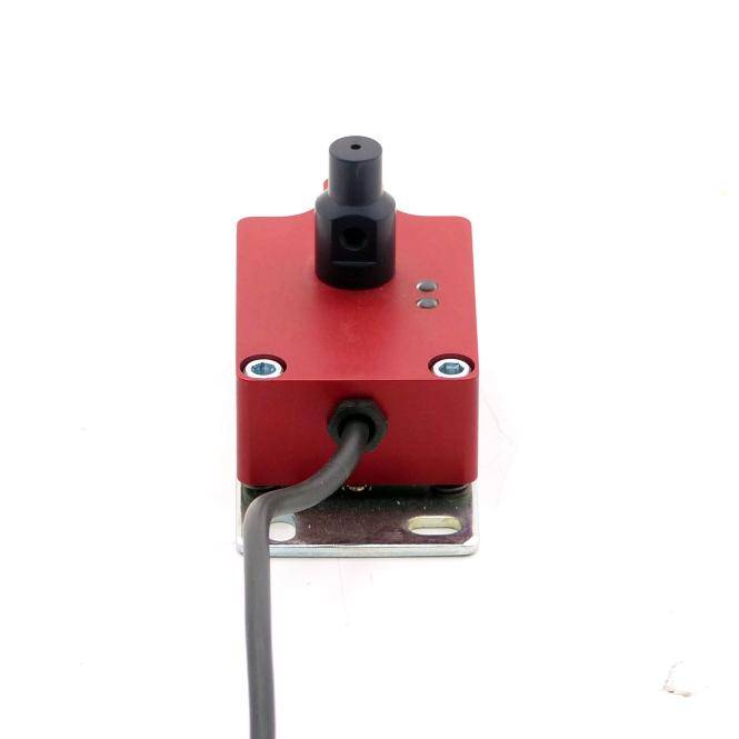 Rote Metalleletrokomponente mit schwarzem Stecker und angeschlossenem Kabel, montiert auf einer kleinen Metallhalterung vor weißem Hintergrund.