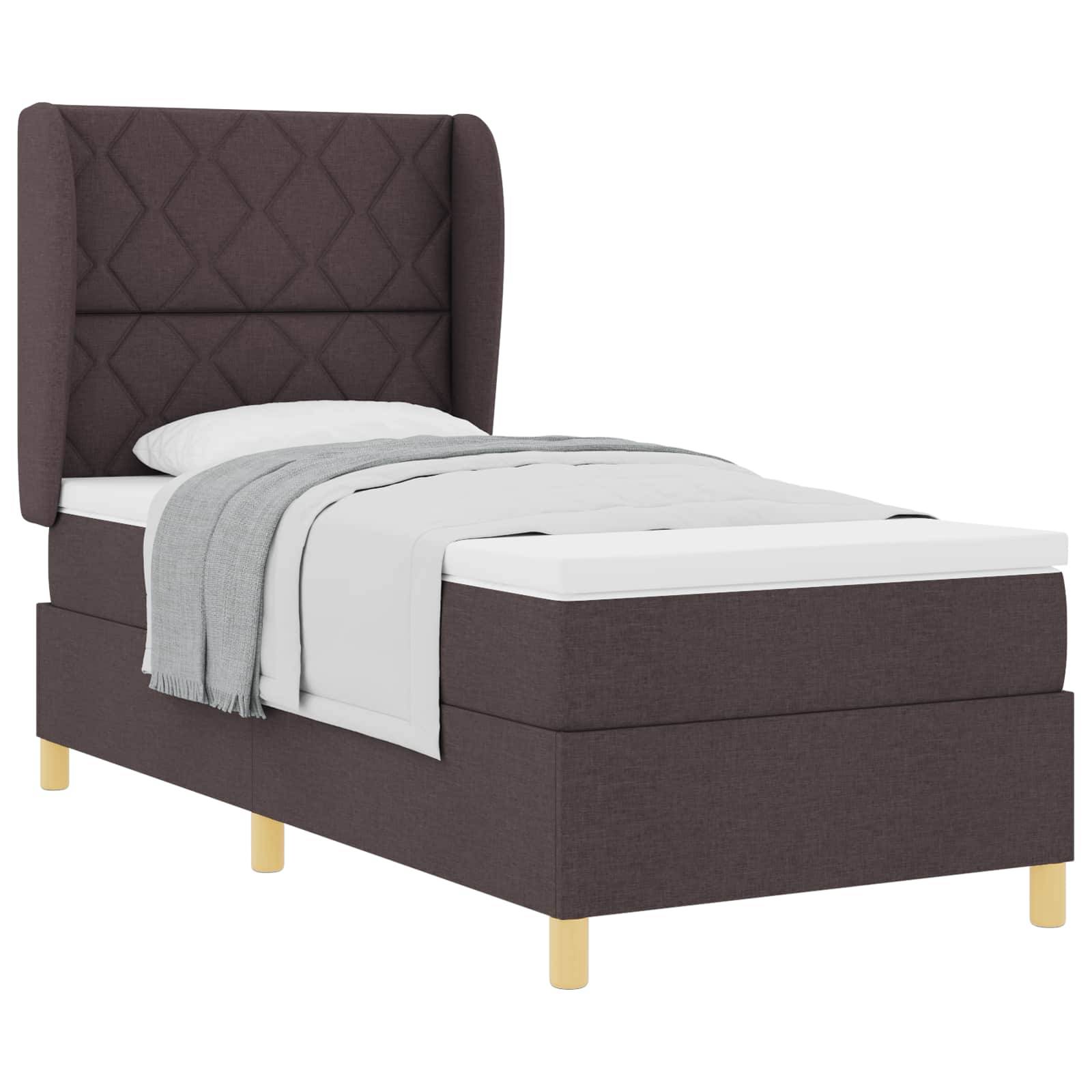 Ein gemütliches Einzelbett mit einem hohen, dunklen Polsterkopfteil, weißer Bettwäsche und einer grauen Decke, gestützt von hellen Holzbeinen.