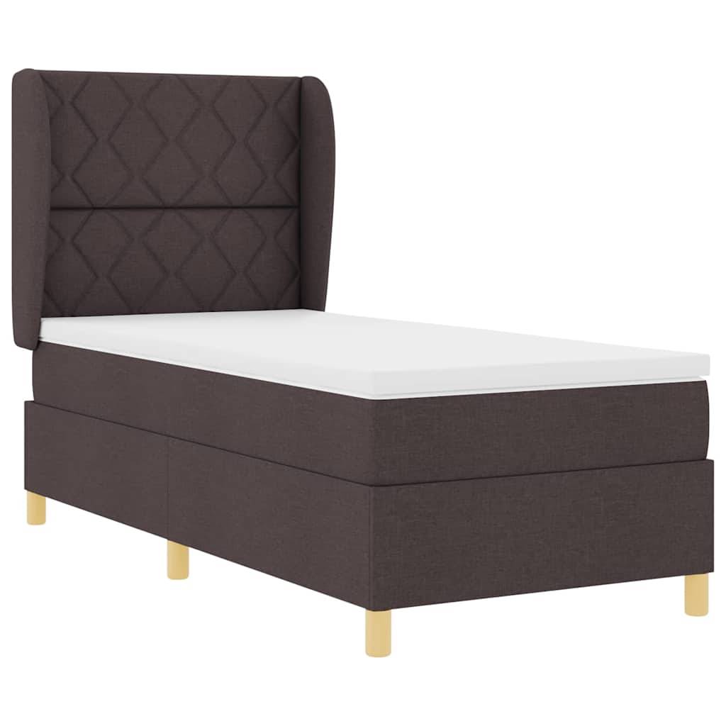 Ein Einzelbett mit einer hohen, gesteppten Kopfstütze und einer weißen Matratze. Das Bett hat vier Holzbeine und keine sichtbare Bettwäsche.