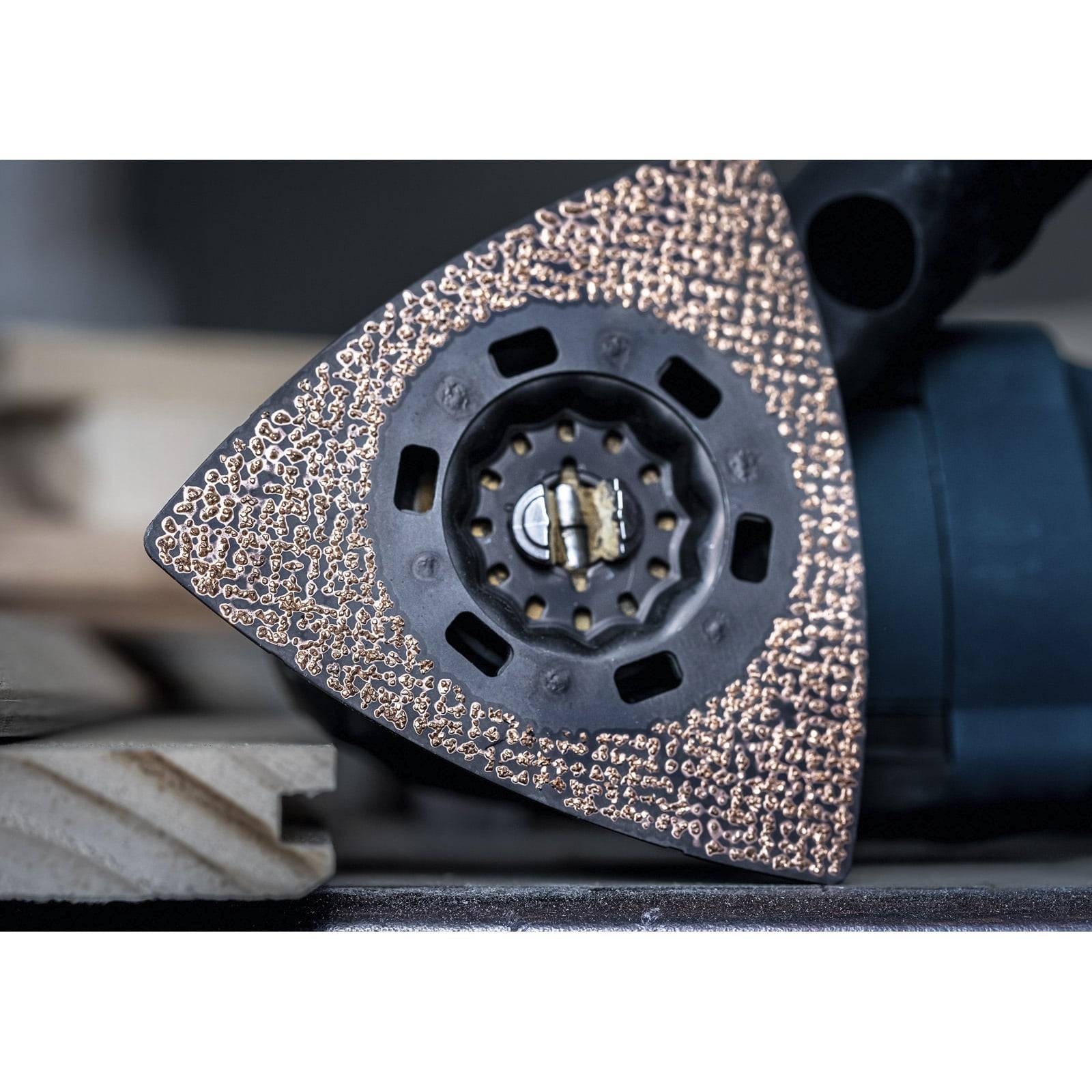 „Eine Nahaufnahme eines strukturierten dreieckigen Schleifrschleifers auf einem Elektrowerkzeug, umgeben von Holzbrettern, was auf eine Holzbearbeitungsaufgabe hindeutet.