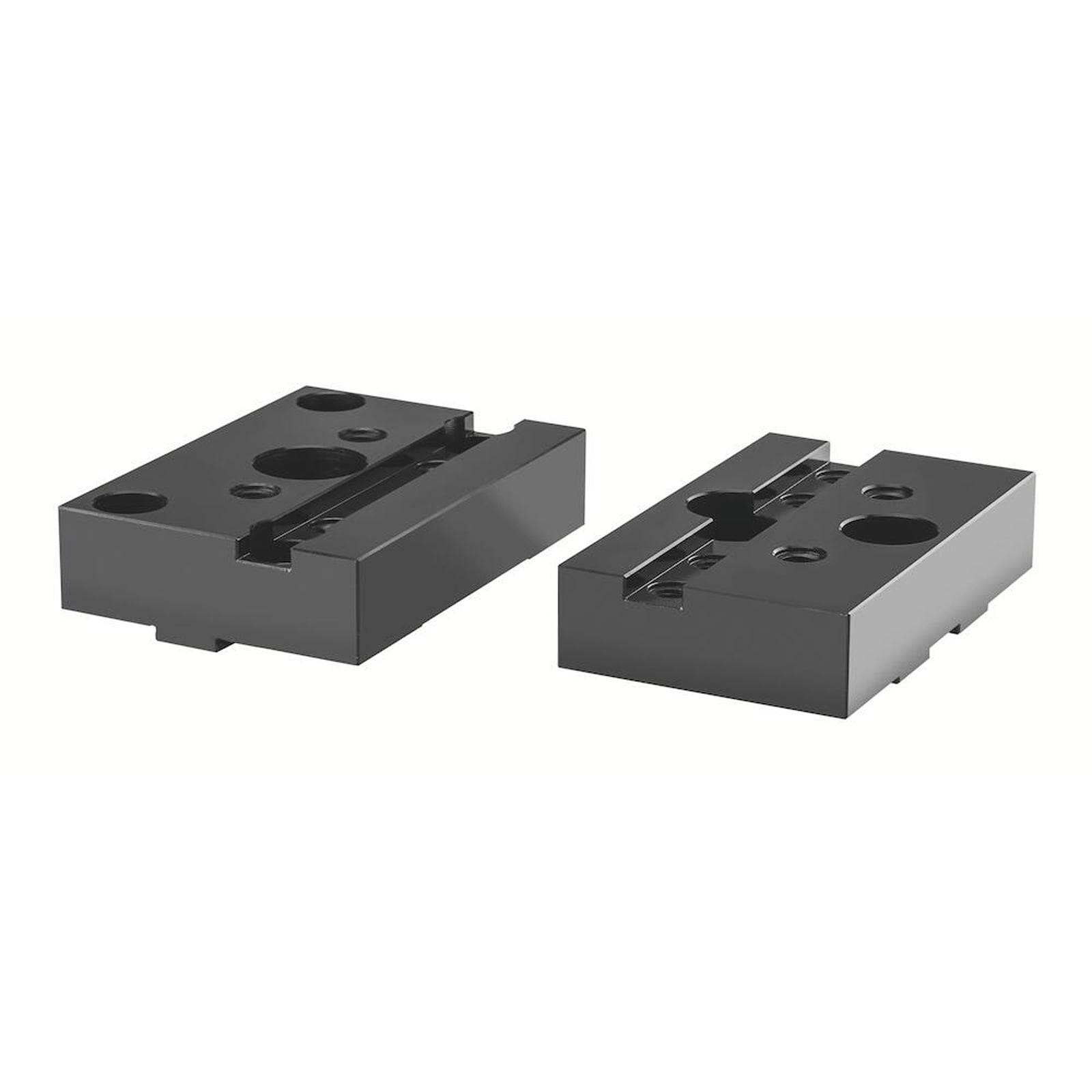 Zwei schwarze Metallblöcke mit verschiedenen Löchern und Schlitzen auf der Oberfläche, möglicherweise mechanische Komponenten oder Befestigungen.