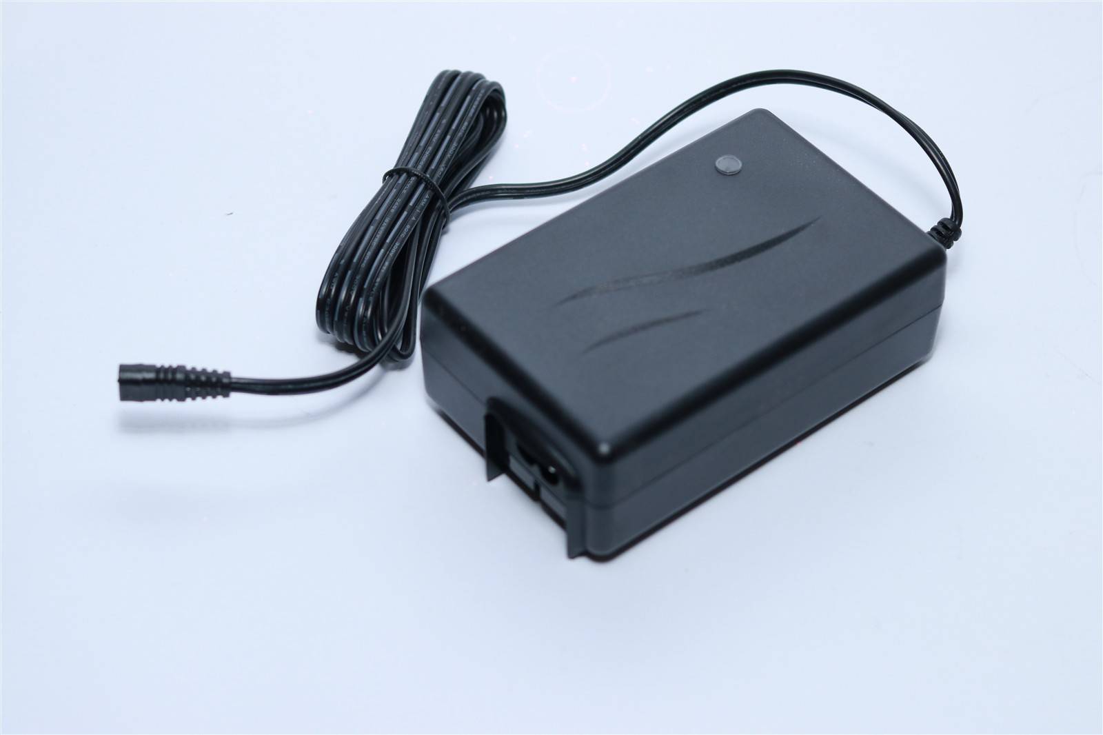 Ein schwarzes Netzteil mit angeschlossenem Kabel liegt auf einer hellen Oberfläche.