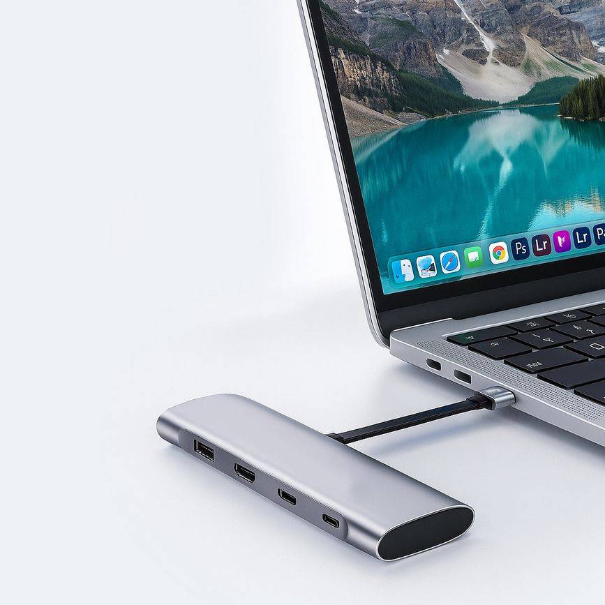 Laptop angeschlossen an einen silbernen USB-C-Hub mit mehreren Anschlüssen auf einer weißen Oberfläche.