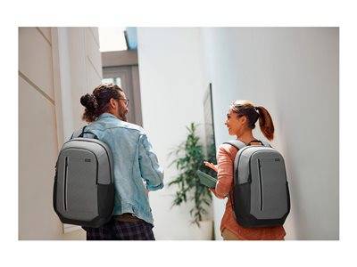 Ein Mann und eine Frau, beide mit einem grauen Rucksack, gehen lächelnd nebeneinander an einem Gebäude vorbei.