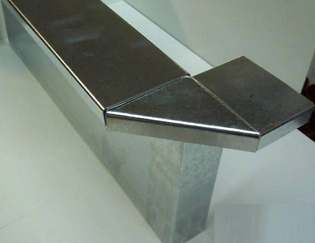 Ein glänzendes silbernes Metallrohr mit rechteckiger Form und einer 90-Grad-Biegung in der Ecke, das Licht reflektiert.