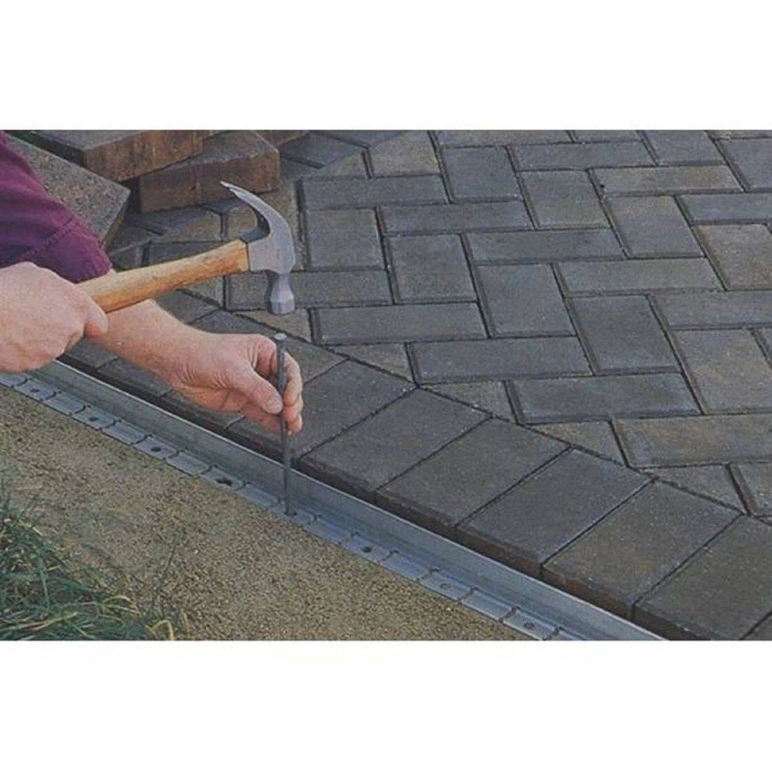 Eine Person nutzt einen Hammer und Meißel, um Pflastersteine auf einer Terrasse anzupassen und sie entlang eines Metallstreifens für präzise Platzierung auszurichten.