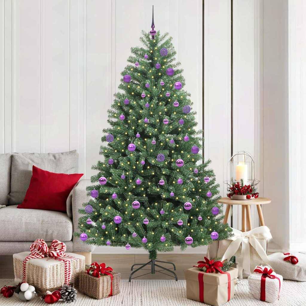 Ein geschmückter Weihnachtsbaum mit lila Kugeln und Lichtern steht in einem Wohnzimmer. Geschenke sind darunter platziert; ein kerzenbeleuchteter Tisch befindet sich in der Nähe.