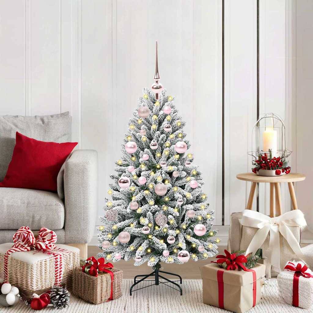 Ein geschmückter Weihnachtsbaum mit silbernen und rosa Ornamenten steht im Wohnzimmer. In der Nähe befinden sich eingewickelte Geschenke, eine Kerze und ein rotes Kissen.