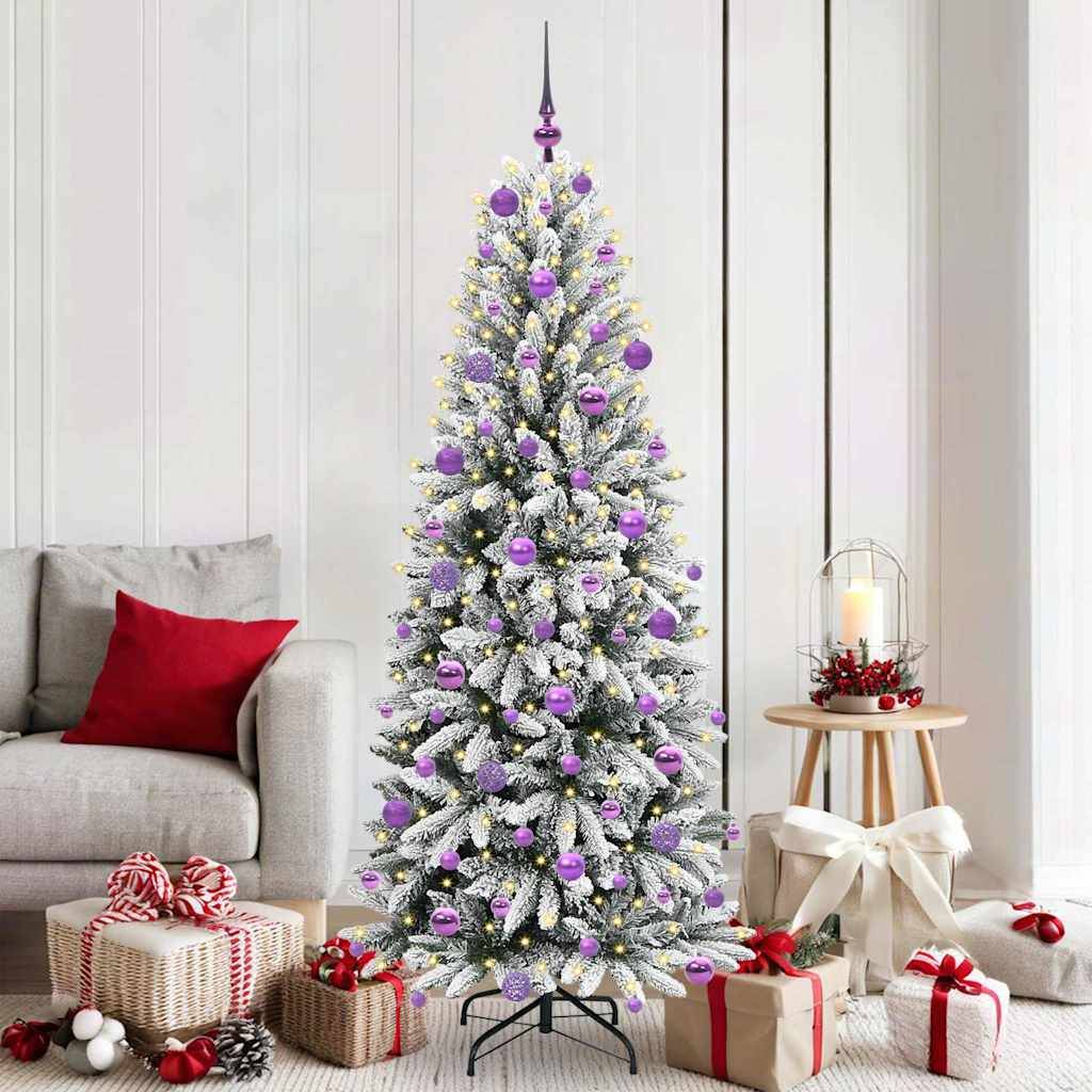 Schneebedeckter Weihnachtsbaum, der mit lila Ornamenten in einem Wohnzimmer geschmückt ist, umgeben von eingewickelten Geschenken, einem Sofa und einer Laternenkerze.