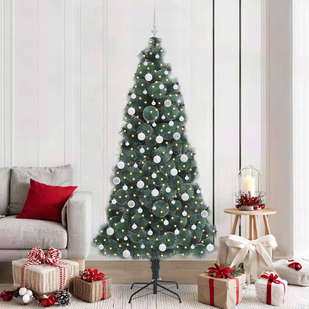 Ein großer, geschmückter Weihnachtsbaum mit silbernen Kugeln und weißen Lichtern steht in einem Wohnzimmer neben einem grauen Sofa und Geschenkboxen.