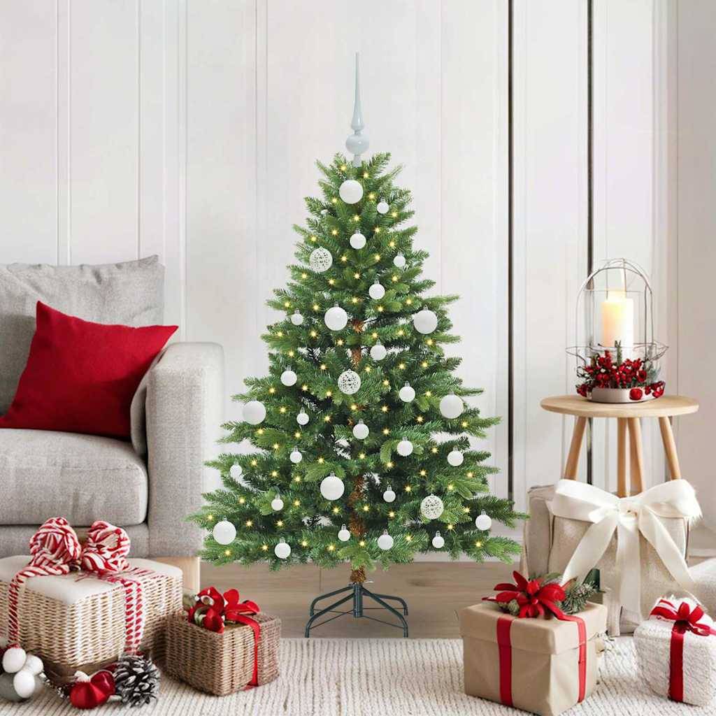 Geschmückter Weihnachtsbaum in einem Wohnzimmer, umgeben von eingewickelten Geschenken und Weihnachtsdekoration neben einem Sofa und einer Kerzenlaterne.