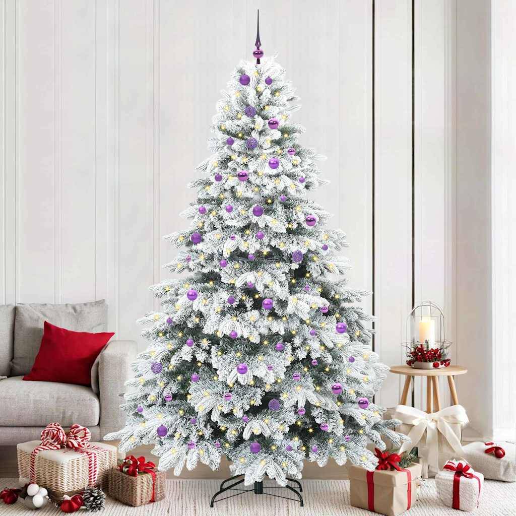 Ein geschmückter Weihnachtsbaum mit weißen, schneeartig aussehenden Ästen, lila und weißen Christbaumkugeln, steht in einem Wohnzimmer. Geschenkkartons befinden sich darunter.