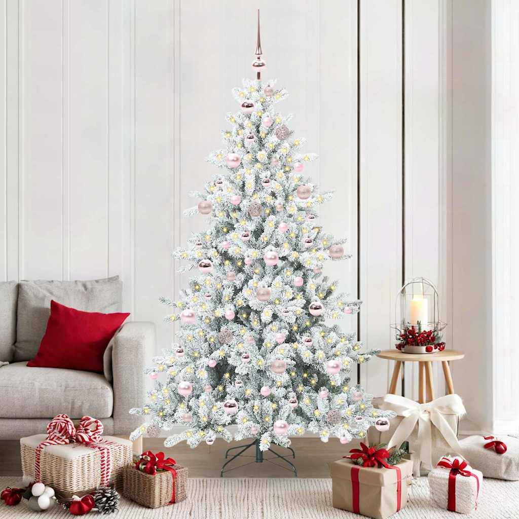 Ein geschmückter weißer Weihnachtsbaum mit Ornamenten und Lichtern steht in einem Wohnzimmer neben einem grauen Sofa und einem kleinen Holztisch mit einer Kerze.