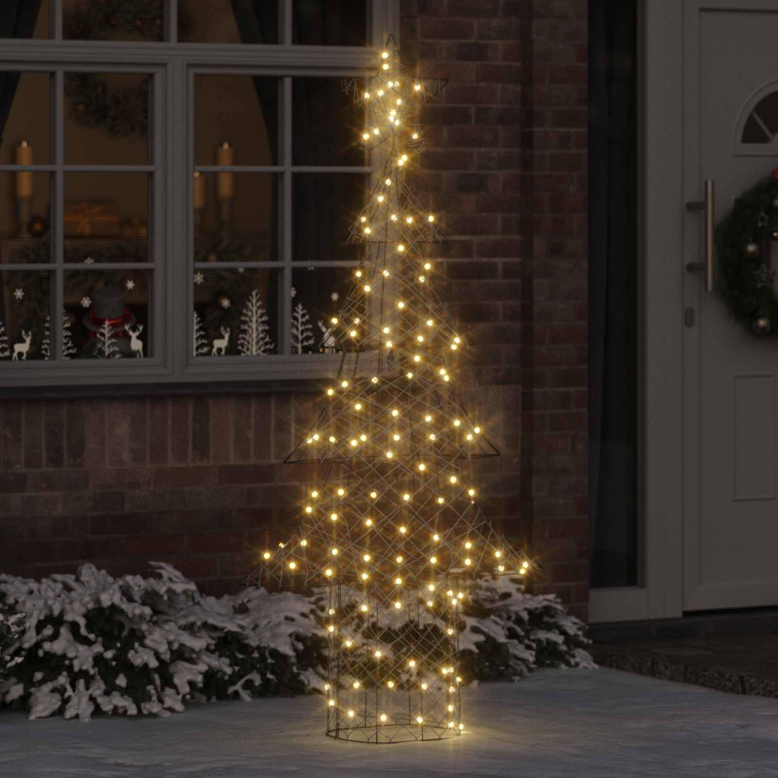 Ein beleuchteter Weihnachtsbaum im Freien vor einem Haus mit Schnee auf dem Boden, im Hintergrund leuchten die Fenster warm.