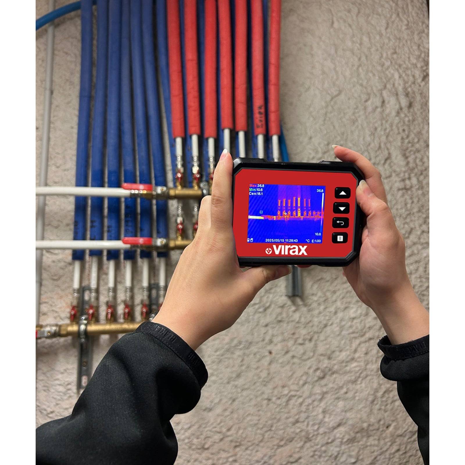 Eine Person hält ein digitales Gerät mit einer Temperaturdiagramm vor einem Netzwerk von roten und blauen Rohrleitungen, möglicherweise zur Diagnose.