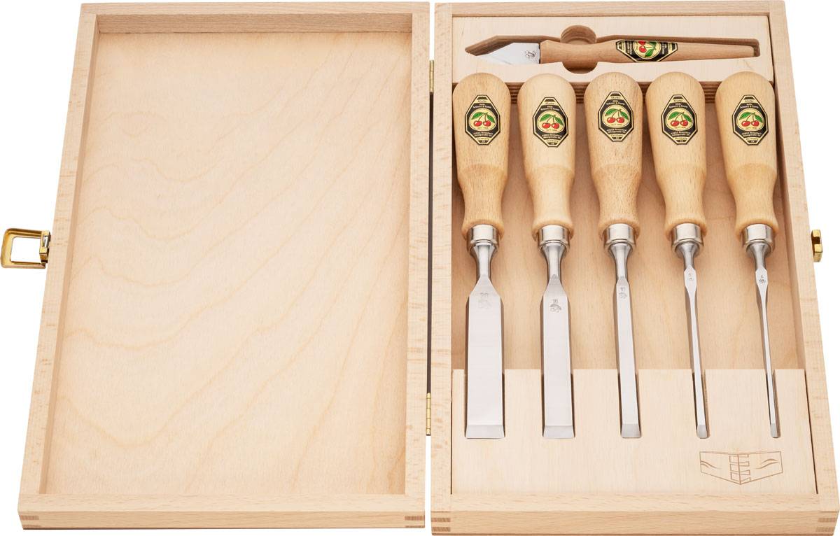 Ein Set von fünf Holzschnitzmeißeln mit Holzgriffen, ordentlich in einem Holzkasten angeordnet, auf einer rustikalen Holzwerkbank platziert.