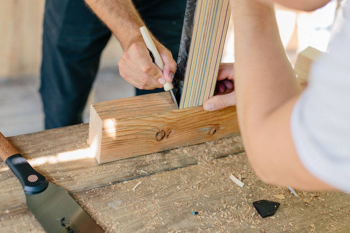 Eine Person verwendet einen Bleistift, um Messwerte auf einer Holzplanke zu markieren, umgeben von Sägespänen, was auf ein laufendes Holzbearbeitungsprojekt hindeutet.