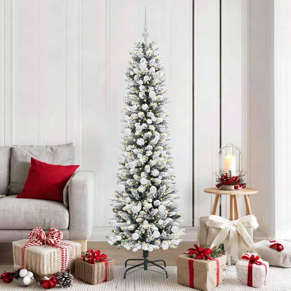 Schneebedeckter künstlicher Weihnachtsbaum in einem hellen Wohnzimmer, umgeben von eingepackten Geschenken, einem Sofa und einem kerzebeleucteten Beistelltisch.