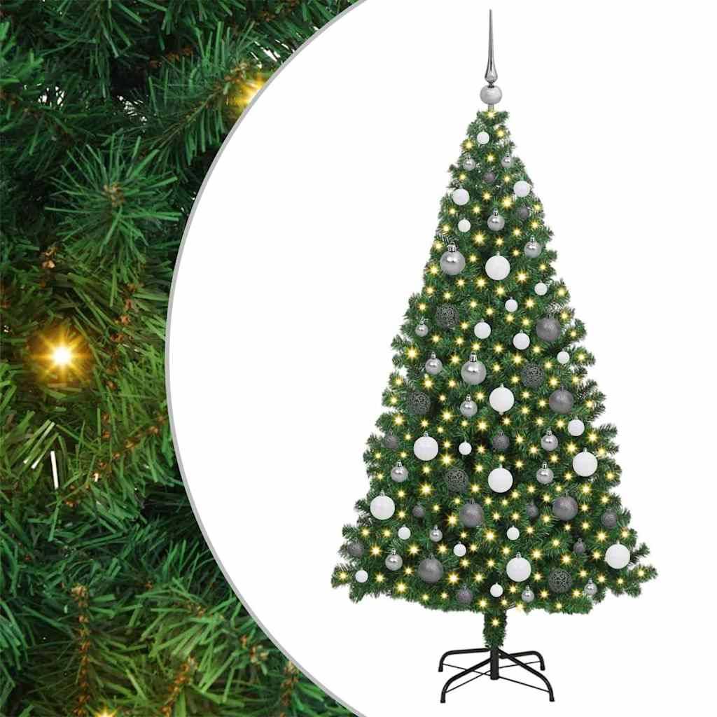 Künstlicher Weihnachtsbaum mit silbernen Christbaumkugeln und warmweißen Lichtern auf einem schwarzen Metallständer, vor einem Hintergrund von grünen Zweigen.