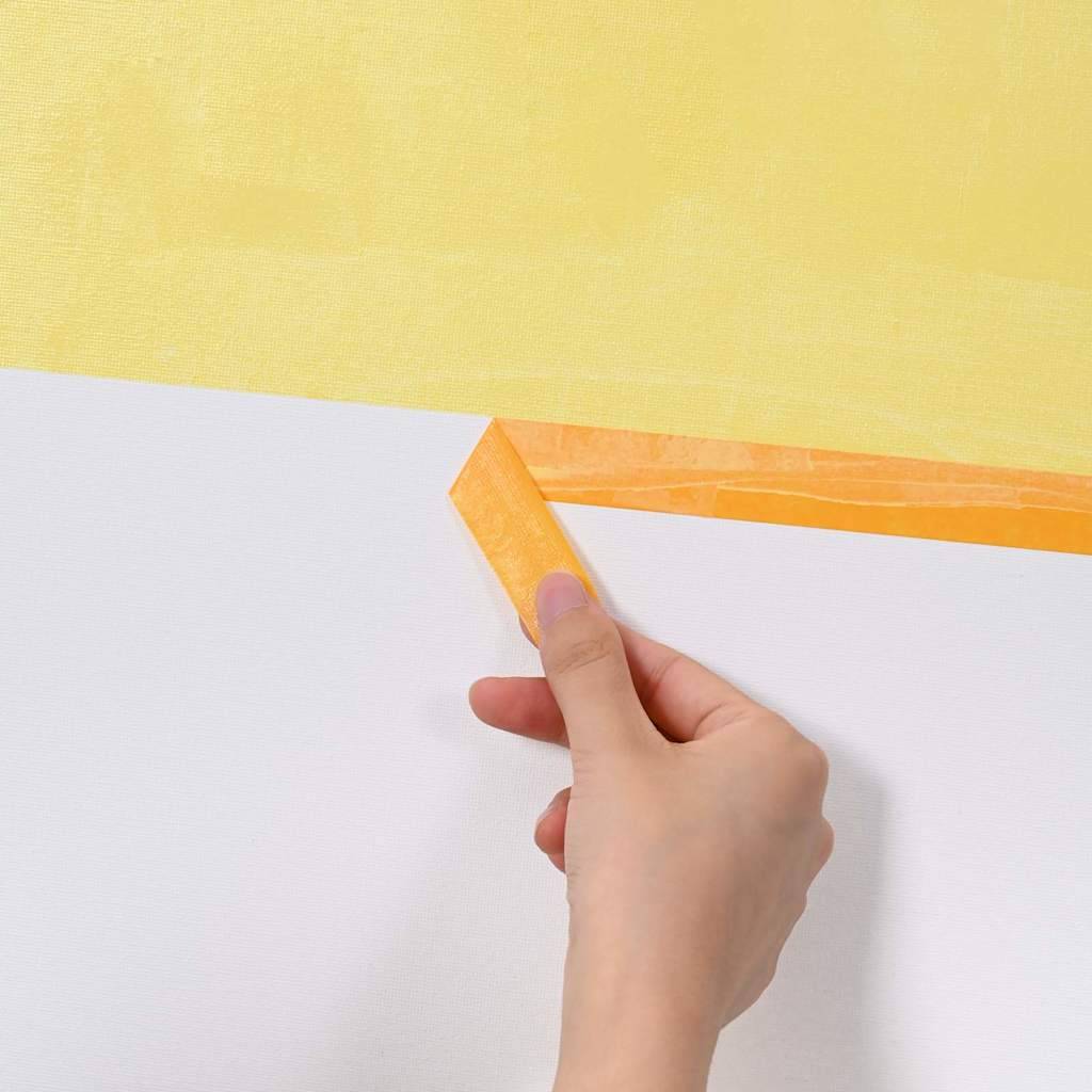 Eine Hand entfernt orangefarbenes Malerkrepp von einer Wand mit einer gelb-weißen Anstrichfläche und enthüllt dabei eine saubere Linie zwischen den Farben.