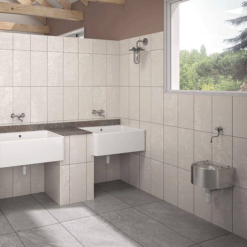 Modernes Badezimmer mit Fliesen, zwei an der Wand befestigten Waschbecken, Duscharmaturem und einem Edelstahlwasserspender in der Nähe eines Fensters mit Blick auf Bäume.