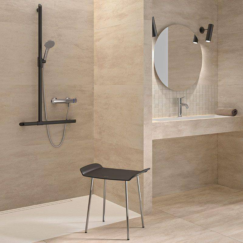 Modernes beiges Badezimmer mit begehbarer Dusche, an der Wand montiertem Waschbecken, rundem Spiegel und schwarzem Hocker.
