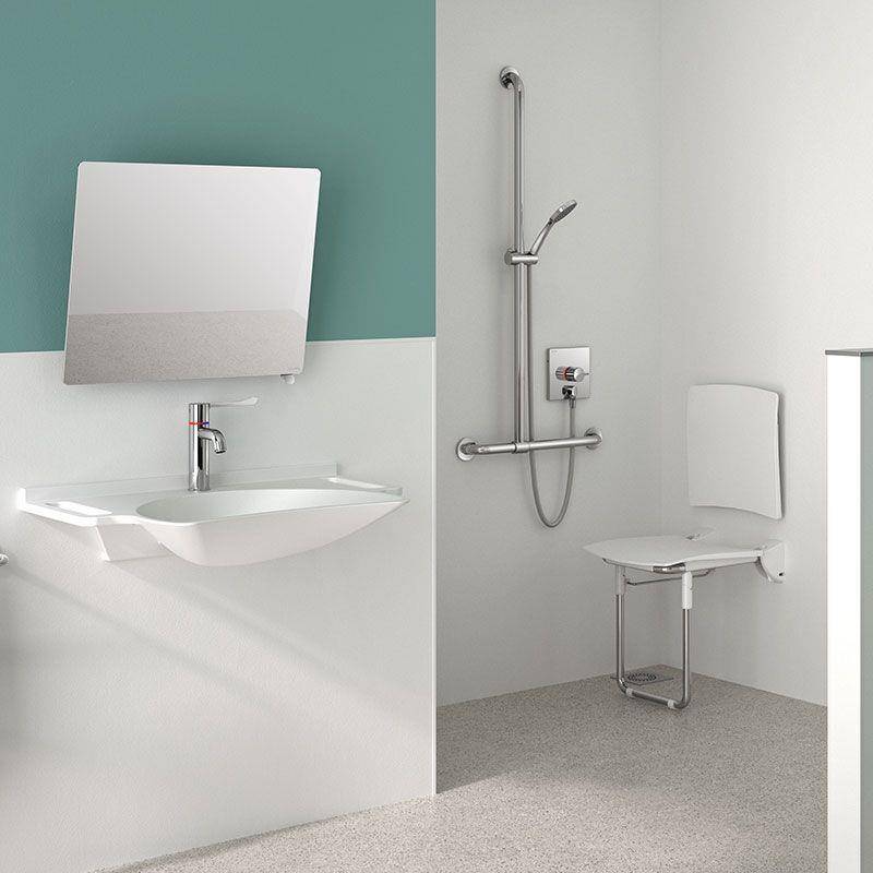 Barrierefreies Badezimmer mit wandmontiertem Waschbecken und Spiegel auf der linken Seite und einem Duschbereich mit Haltegriffen und klappbarem Sitz auf der rechten Seite.