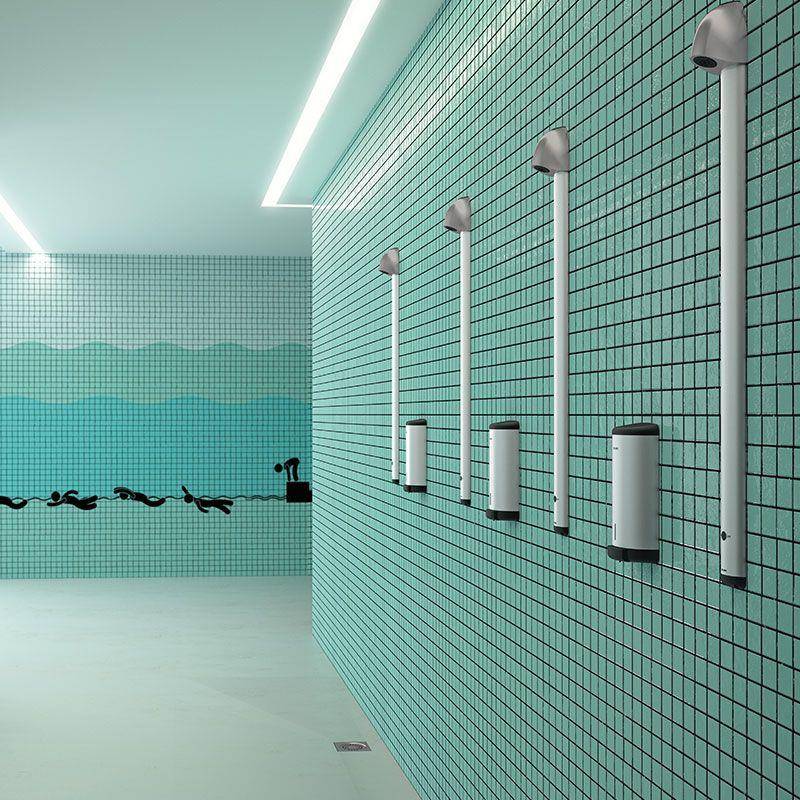 Leeres Hallenschwimmbad mit gefliesten Wänden, Duschköpfen und wandgestützten Spendern, was auf einen Umkleide- oder Waschbereich hindeutet.