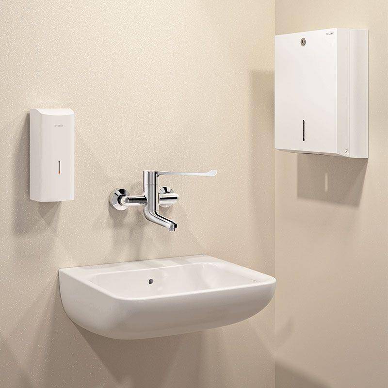 Wandhängeres weißes Waschbecken mit verchromtem Wasserhahn zwischen zwei weißen Spendern in einem minimalistischen Badezimmer.