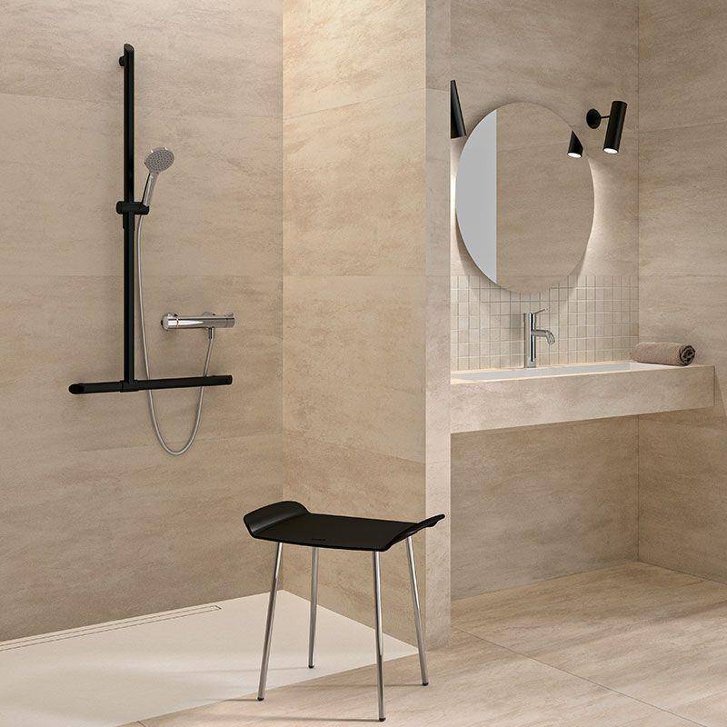 Modernes beiges Badezimmer mit begehbarer Dusche, an der Wand montiertem Waschbecken und rundem Spiegel, sowie einem schwarzen Hocker im Vordergrund.