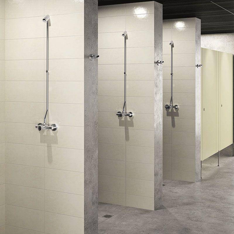 Öffentlicher Duschbereich mit drei gefliesten Kabinen, jede mit wandmontierten Duschköpfen und Bedienelementen; Toilettentrennwände sind auf der rechten Seite sichtbar.