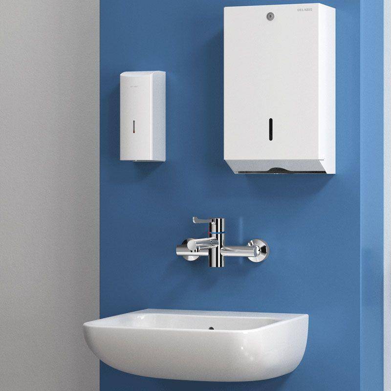Moderner Badezimmerwaschbereich mit wandmontiertem Wasserhahn, weißem Becken und zwei weißen Spendern an einer blauen Wand.