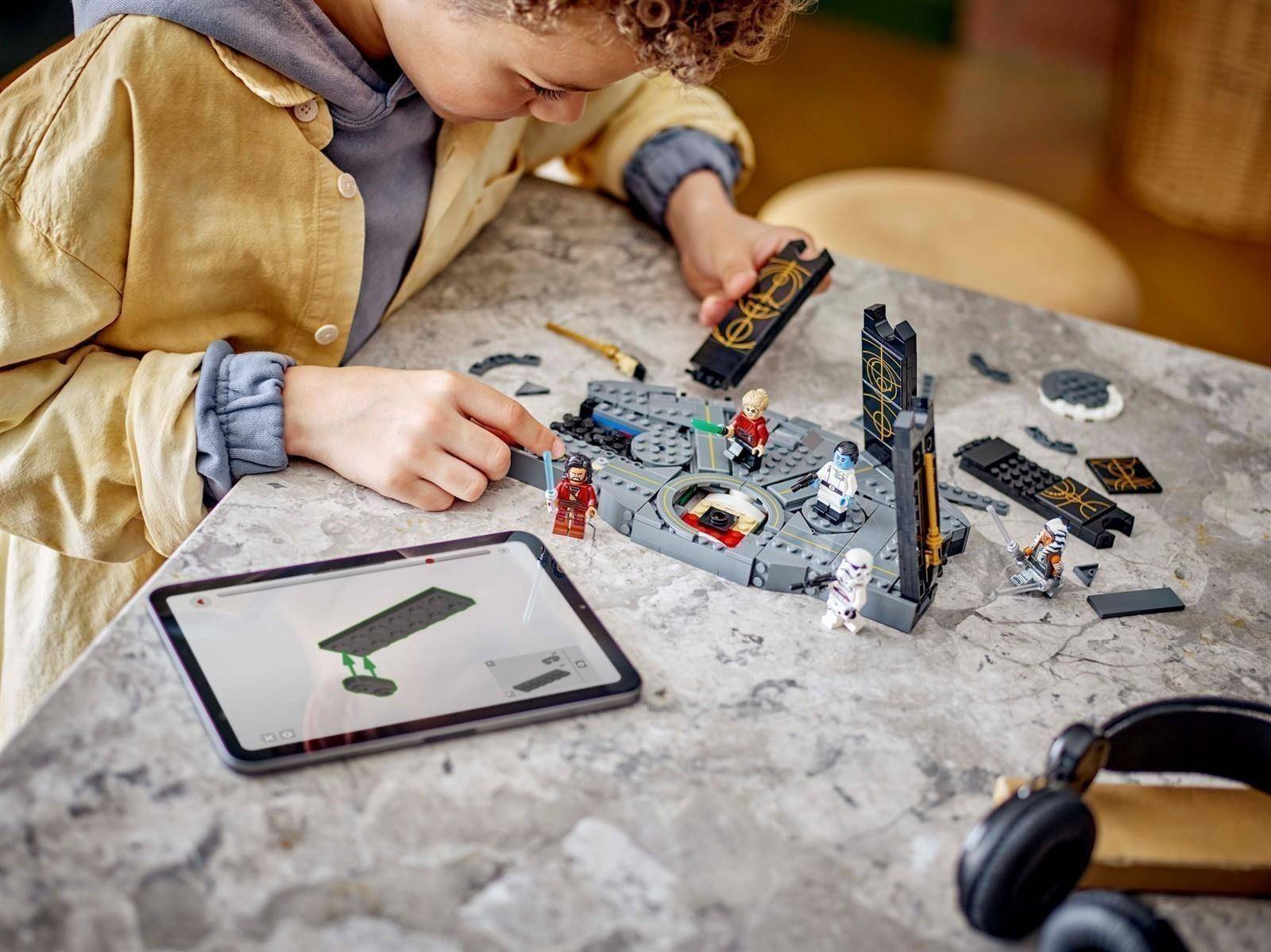 Ein Kind baut eine LEGO Star Wars Szene an einem Tisch, während es Anweisungen auf einem Tablet befolgt.
