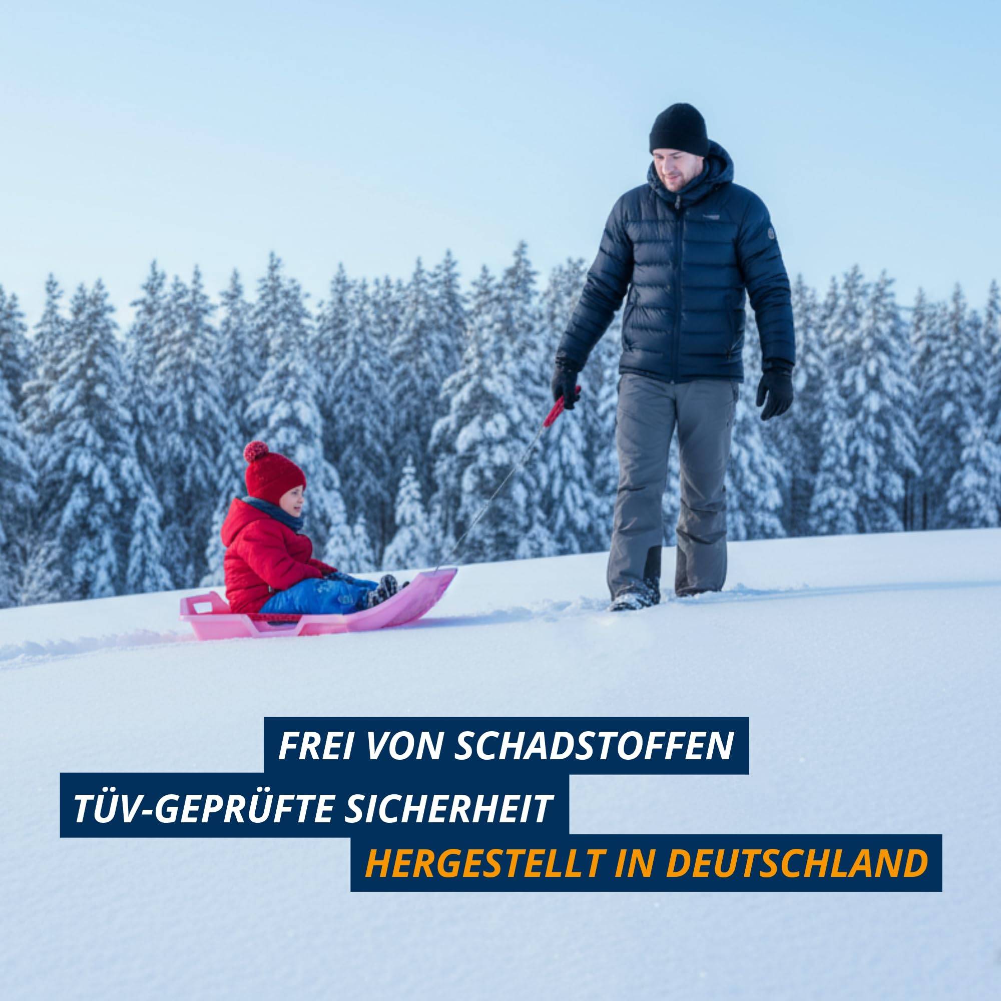 Ein Mann führt ein Kind auf einem Schlitten einen verschneiten Hang mit Kiefern im Hintergrund hinunter. Text: 'Frei von Schadstoffen', 'TÜV-geprüfte Sicherheit', 'Hergestellt in Deutschland'.