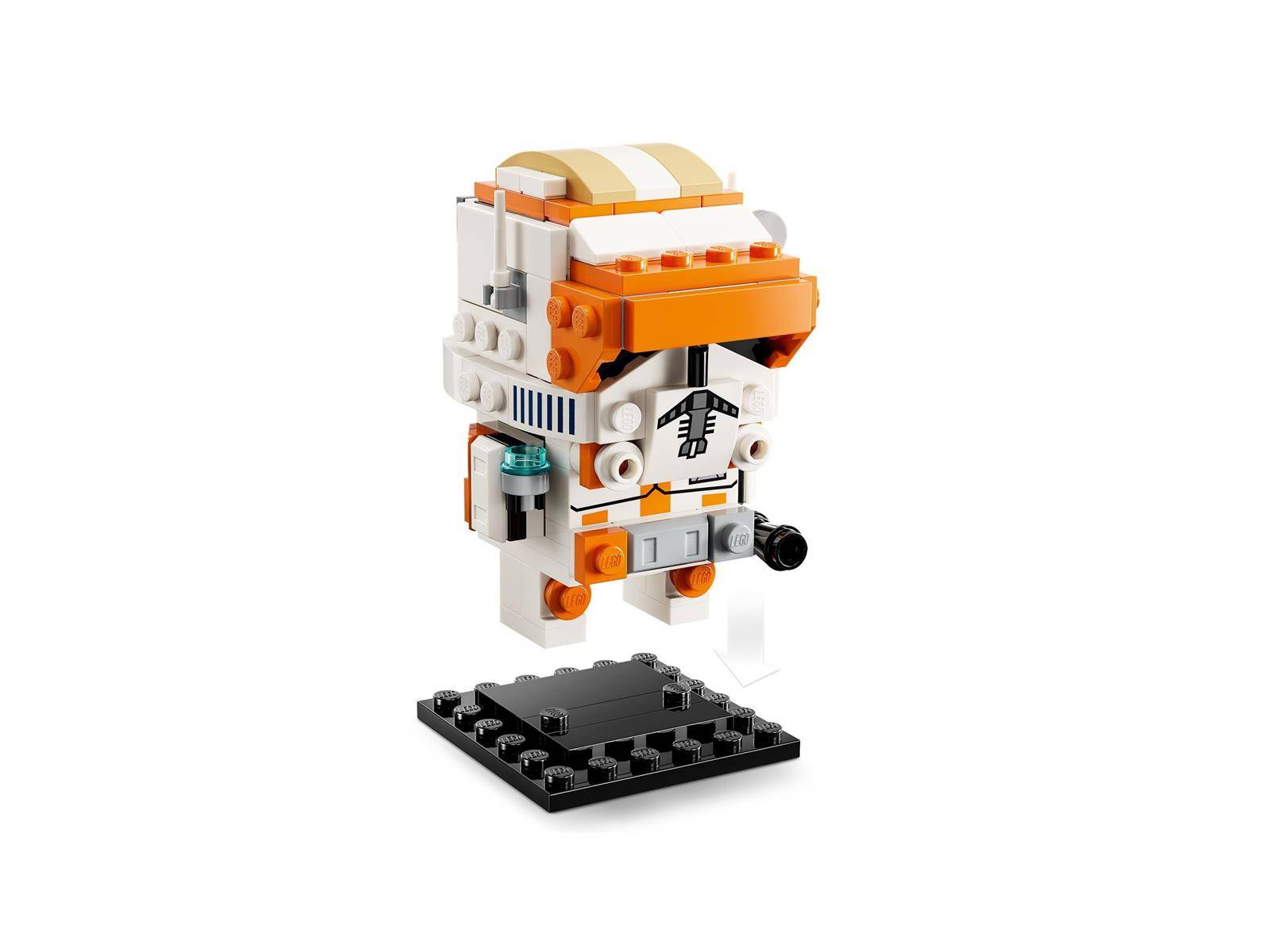 Eine kleine orange-weiße LEGO-ähnliche Roboter- oder Astronautenfigur steht auf einem schwarzen Sockel vor weißem Hintergrund.