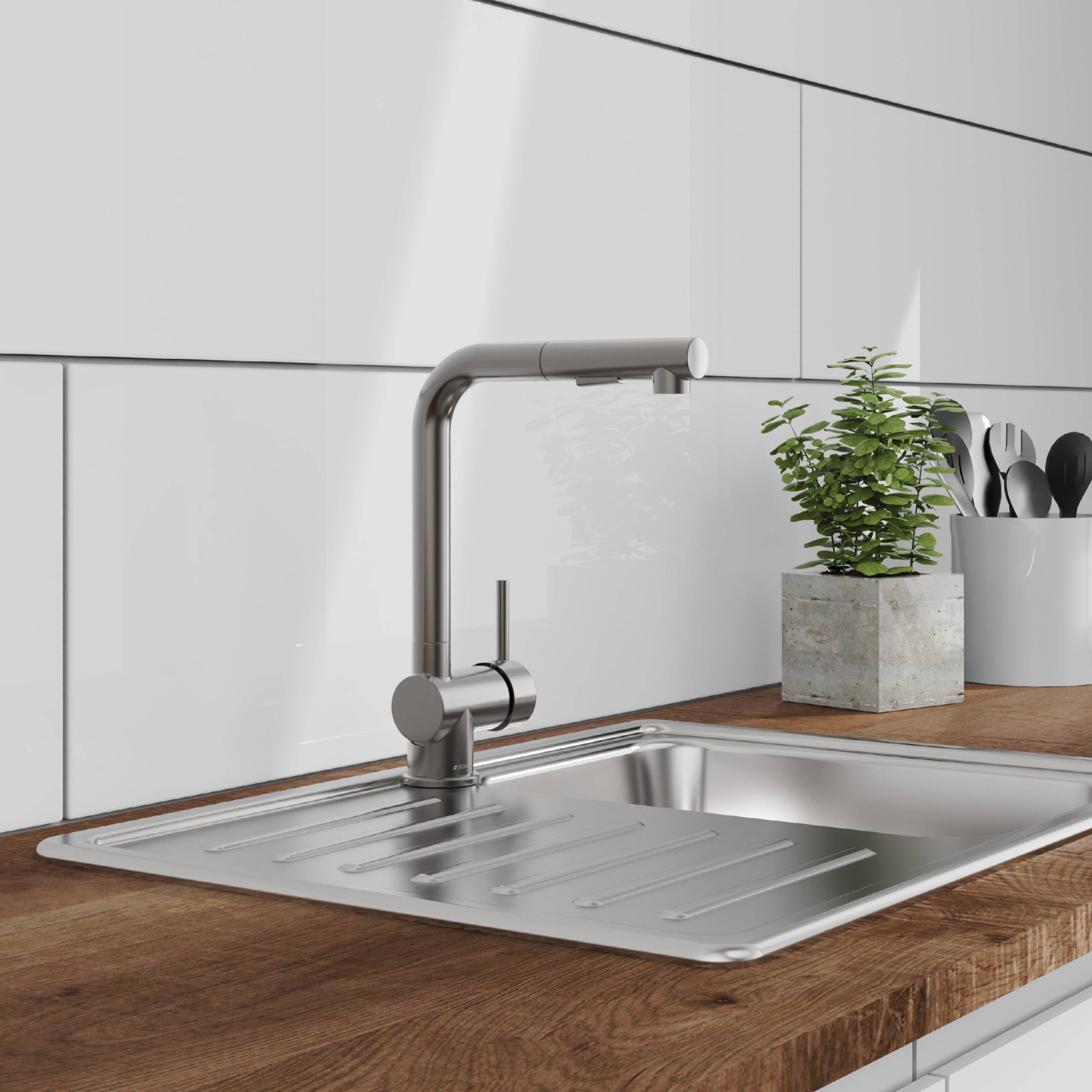 Ein moderner Küchenspülstein mit einem eleganten Metallarmaturen auf einer Holzarbeitsfläche, vor einer weißen gefliesten Rückwand. Eine Topfpflanze und Küchenutensilien befinden sich in der Nähe.