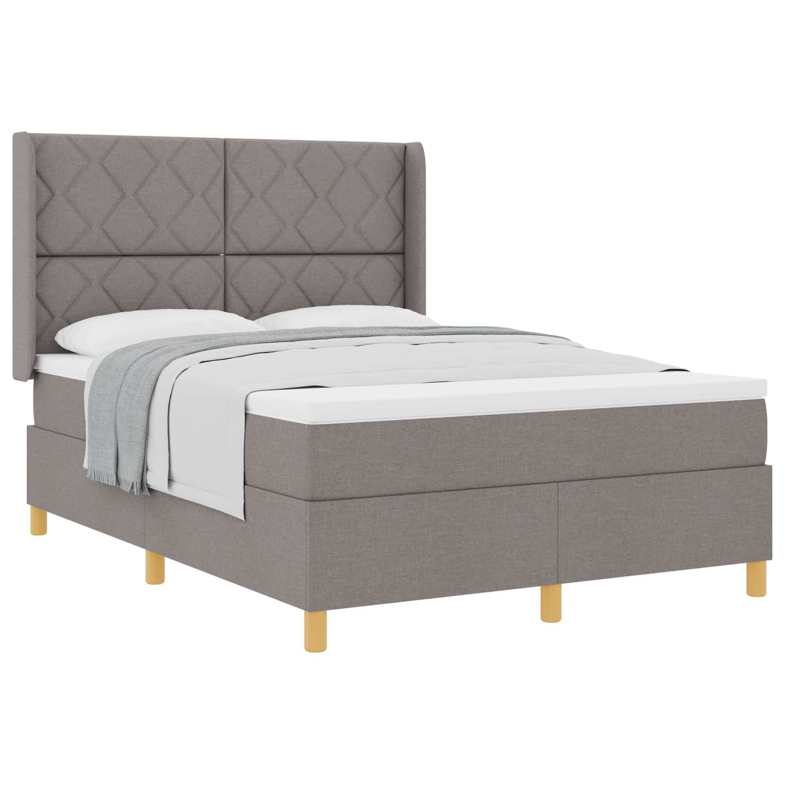 Ein graues gepolstertes Bett mit einer gesteppten Kopfwand, weißer Bettwäsche und einer hellgrauen Decke, die darüber drapiert ist. Das Bett hat Holzbeine.