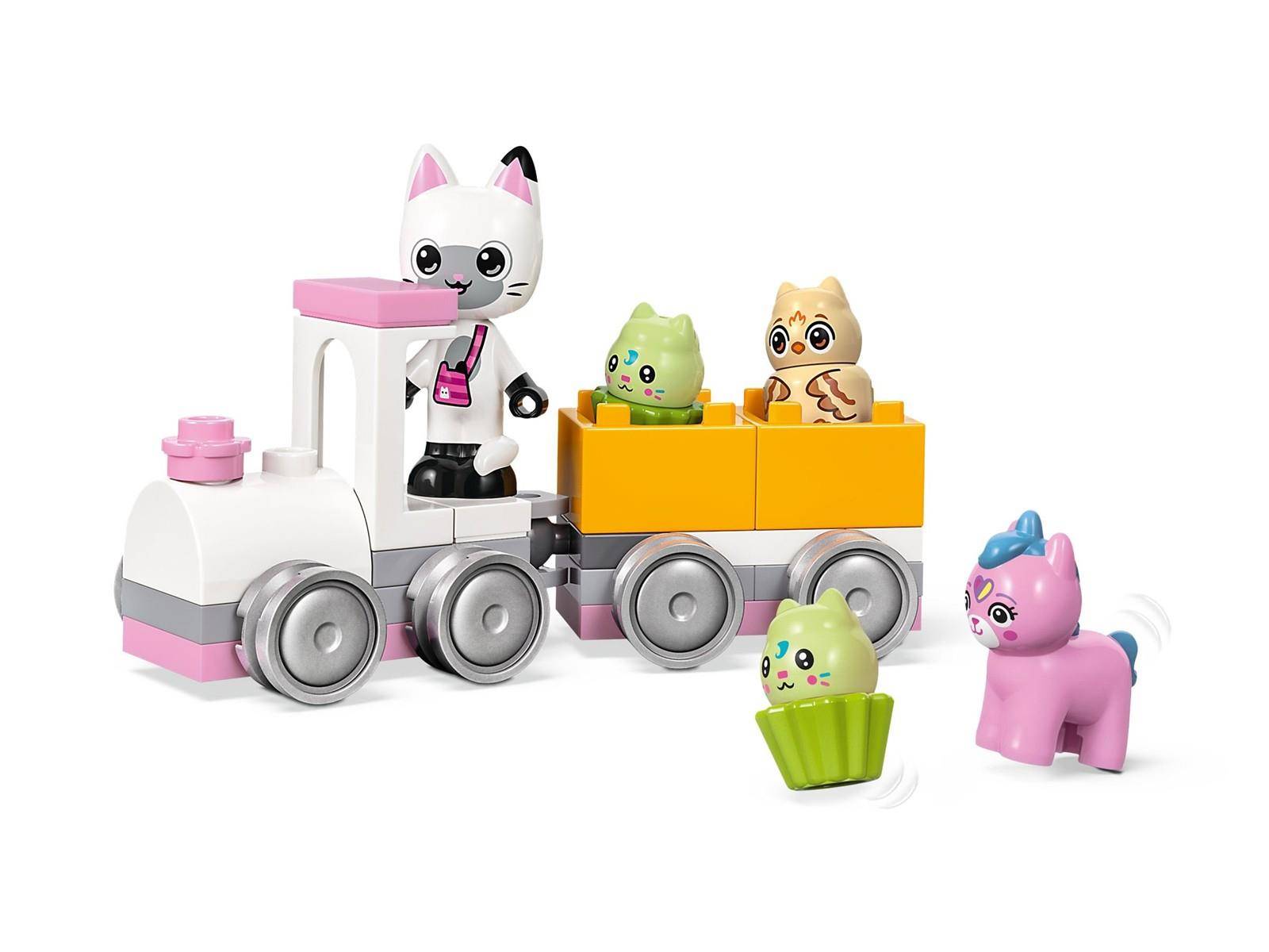 Spielzeugtierzug mit einer weißen Katze als Fahrer, die einen orangefarbenen Wagen mit zwei Küken zieht; ein grünes Küken und ein rosa Pony stehen daneben auf weißem Hintergrund.