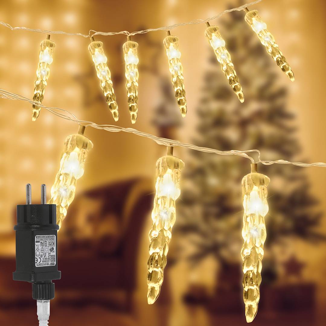 Warmweiße Eiszapfen-Lichterkette auf einem Kabel, mit einem schwarzen Steckeradapter vor einem unscharfen, festlichen Hintergrund.