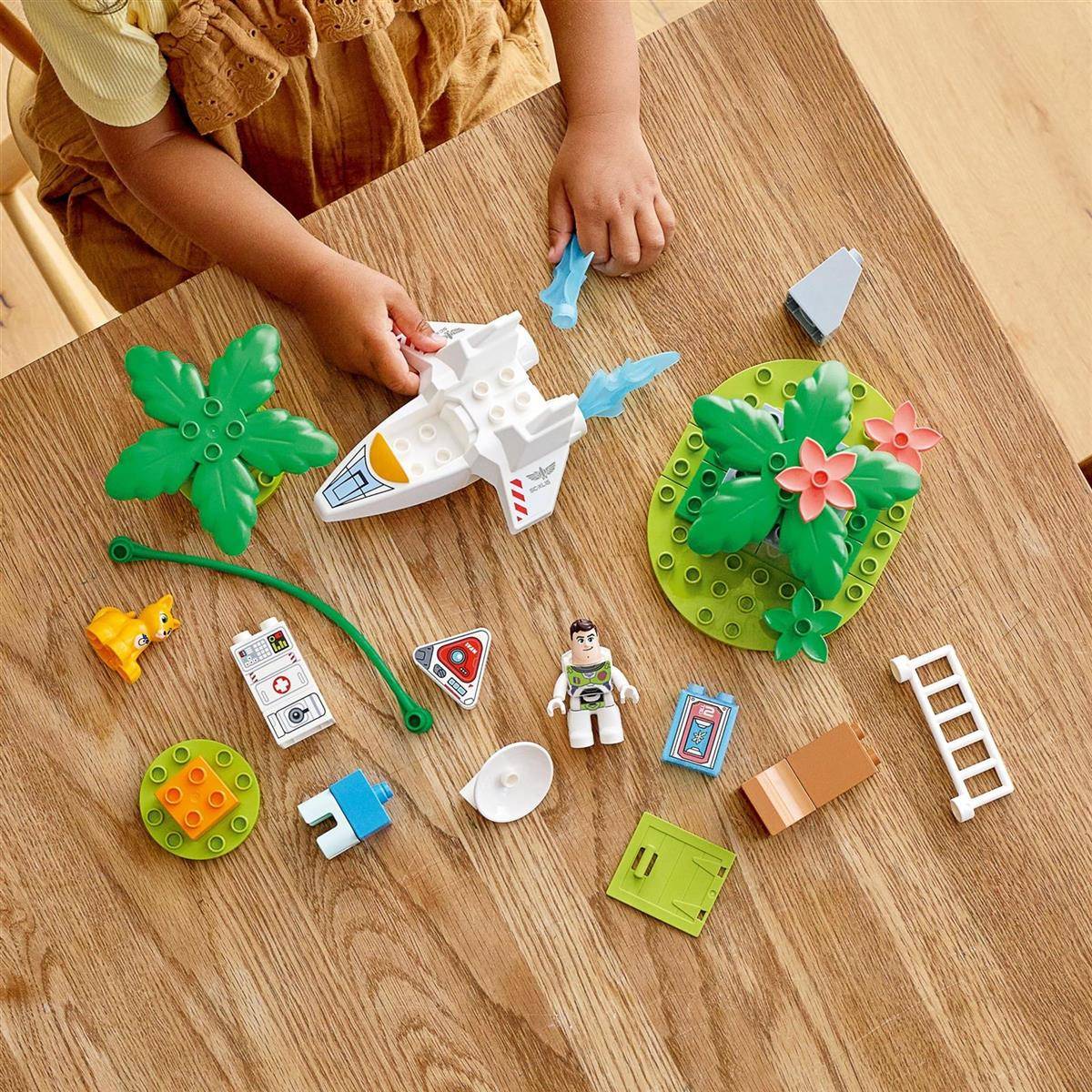 Ein Kind baut Spielbausteine zusammen, darunter eine kleine Rakete, Blätter und Blumen, auf einem Holztisch.