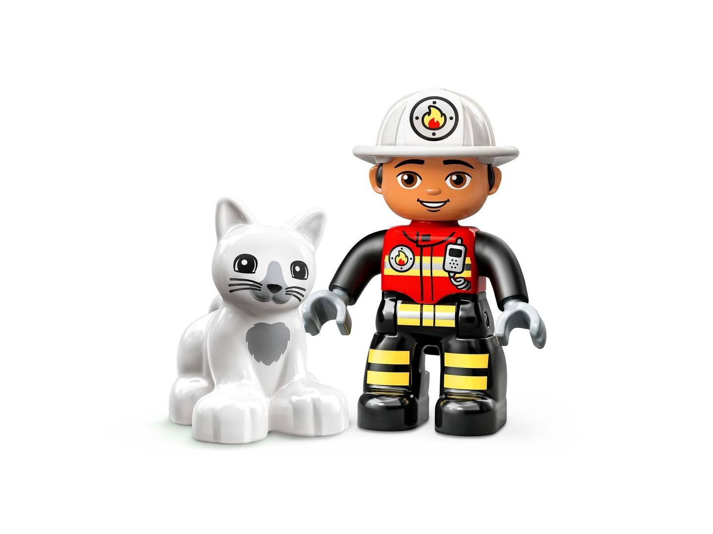 Eine Spielzeugfeuerwehrmannfigur steht neben einer weißen Katzenfigurine auf einem einfachen Hintergrund.