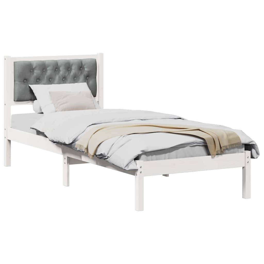 Ein weißes Holz-Einzelbett mit einem grau gepolsterten Kopfteil, ordentlich bezogen mit weißer Bettwäsche und einem beigen Überwurf, der am Fußende drapiert ist.