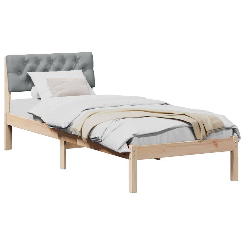 Ein Holz-Einzelbett mit einem grauen gepolsterten Kopfteil, weißer Bettwäsche und einer beigen Decke, von schräg gesehen.