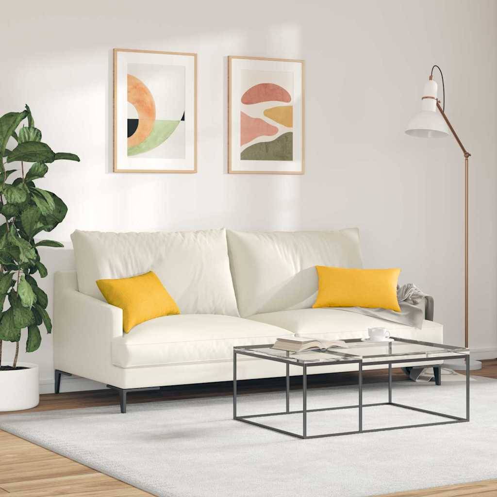 Ein modernes Wohnzimmer mit einem weißen Sofa, zwei gelben Kissen, abstrakter Wandkunst, einer Zimmerpflanze und einer Stehlampe, die eine gemütliche Atmosphäre schafft.