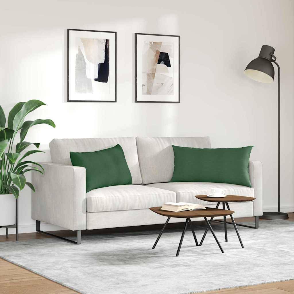 Ein modernes Wohnzimmer mit einem weißen Sofa, zwei grünen Kissen, einem hellgrauen Teppich und einem kleinen Couchtisch. Zwei abstrakte Kunstwerke hängen an der Wand.