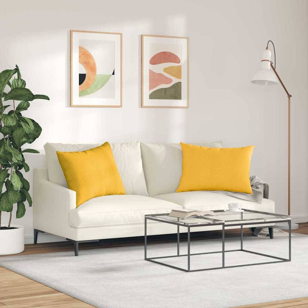 Ein modernes Wohnzimmer mit einem weißen Sofa, zwei gelben Kissen, abstrakter Kunst an der Wand, einer hohen Lampe, einer Pflanze und einem Glaskaffeetisch.