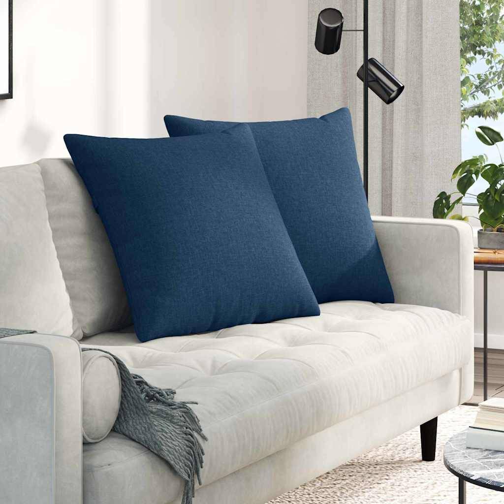 Ein modernes Wohnzimmer zeigt ein hellgraues Sofa mit zwei großen dunkelblauern Kissen, eine Stehlampe und einen Blick auf ein Fenster mit natürlichem Licht.