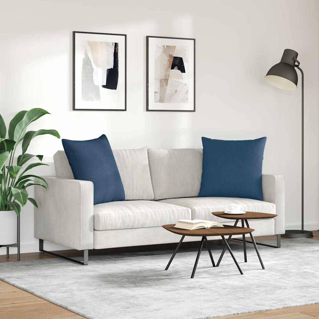 Ein modernes Wohnzimmer mit weißem Sofa, blauen Kissen, abstrakter Kunst an der Wand, Topfpflanzen und einem kleinen hölzernen Couchtisch auf einem grauen Teppich.